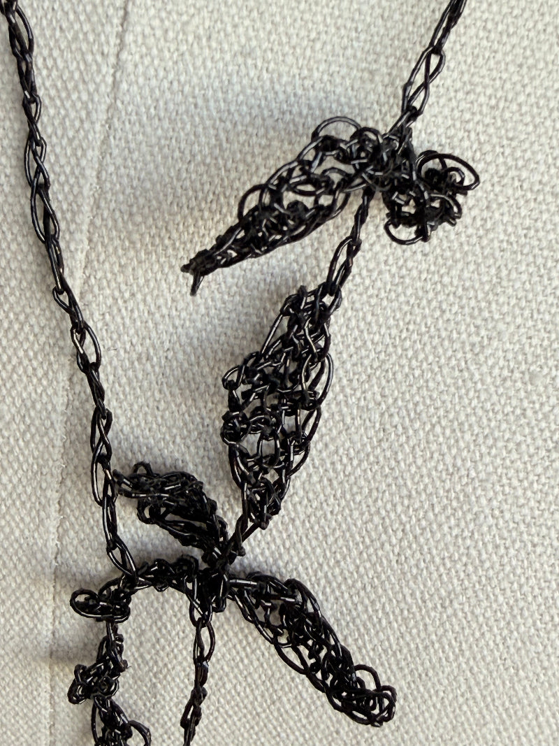 A close-up of a black metal chain necklace laid on a textured off-white fabric background.